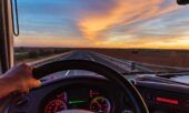 View from a truck driver where you can see the speedometer and fuel gauge as he drives down a highway during a sunset.