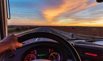 View from a truck driver where you can see the speedometer and fuel gauge as he drives down a highway during a sunset.